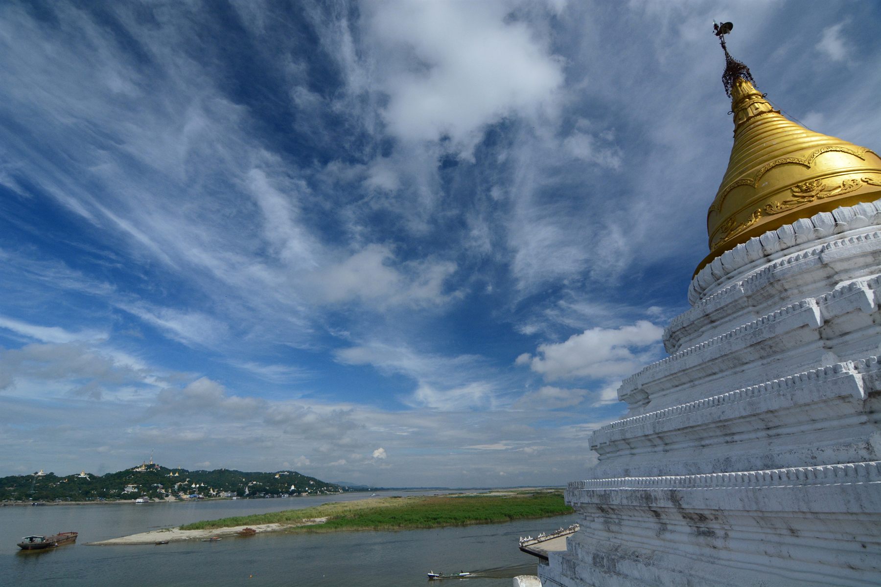 Gilded white stupa overlooking a wide river with sandbanks