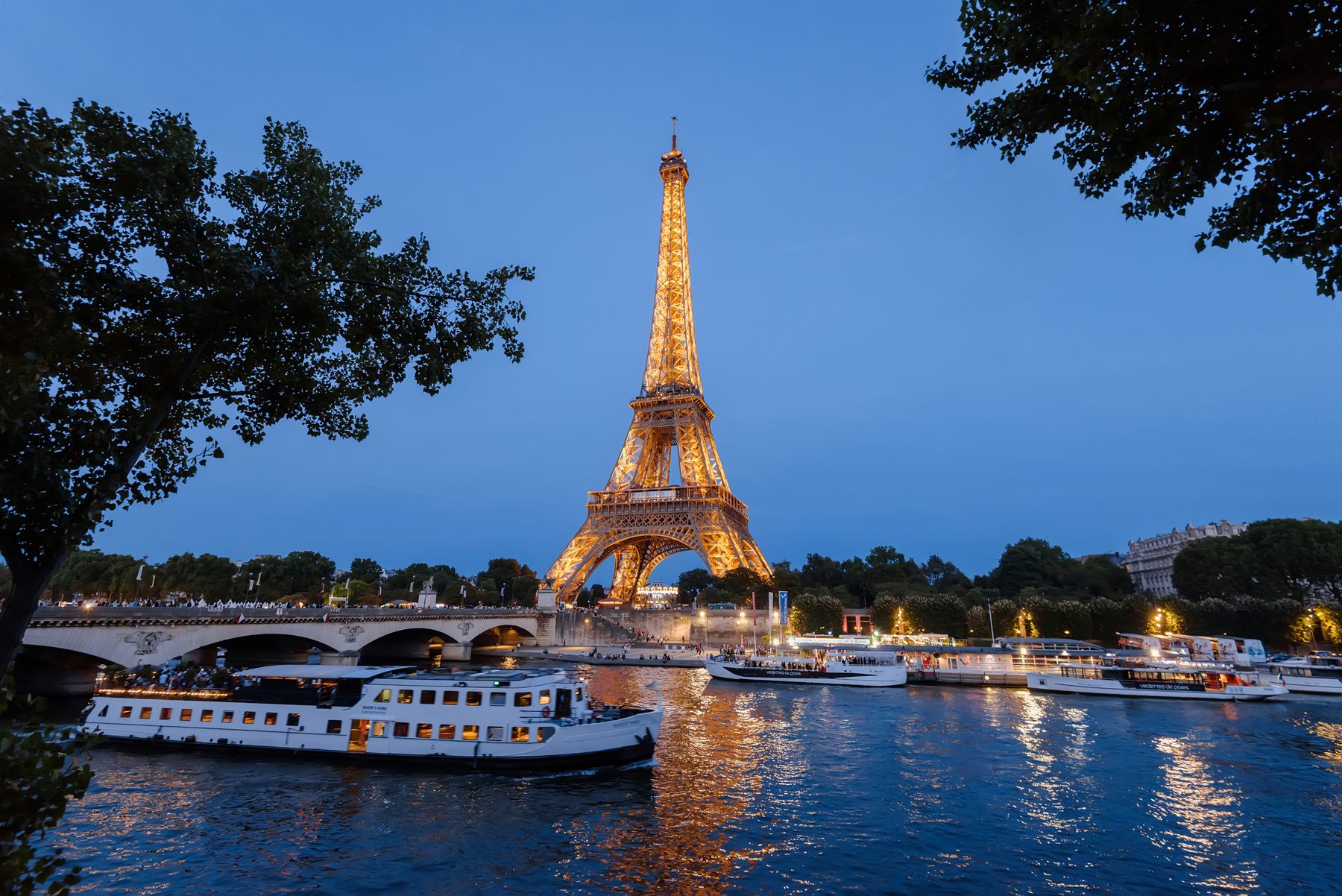 Eiffel Tower lit at dusk above river boats on the Seine